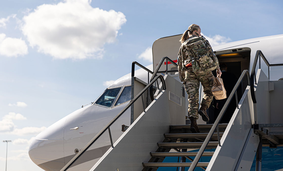 Kvindelig soldat i uniform går op af en mobil trappe for at gå ombord i en mindre flyvemaskine.